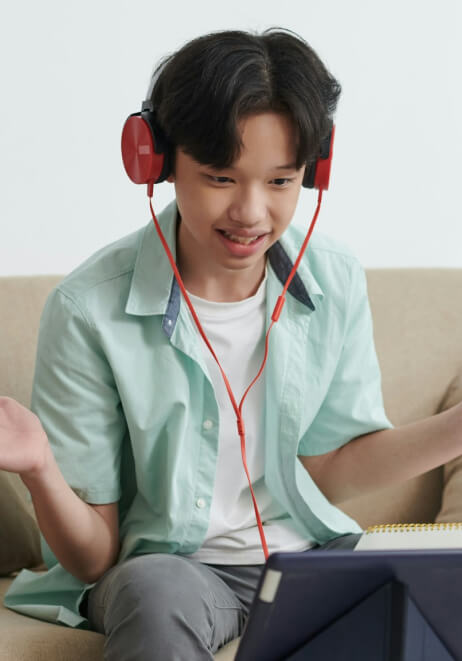 A person wearing red headphones and a light green shirt sits on a couch, smiling and gesturing while looking at a tablet.
