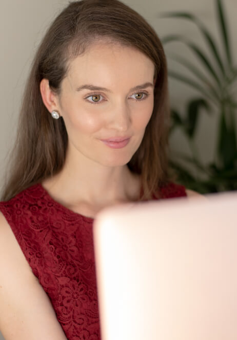 Lauren Crumlish looks at a computer screen, with a green plant in the background.