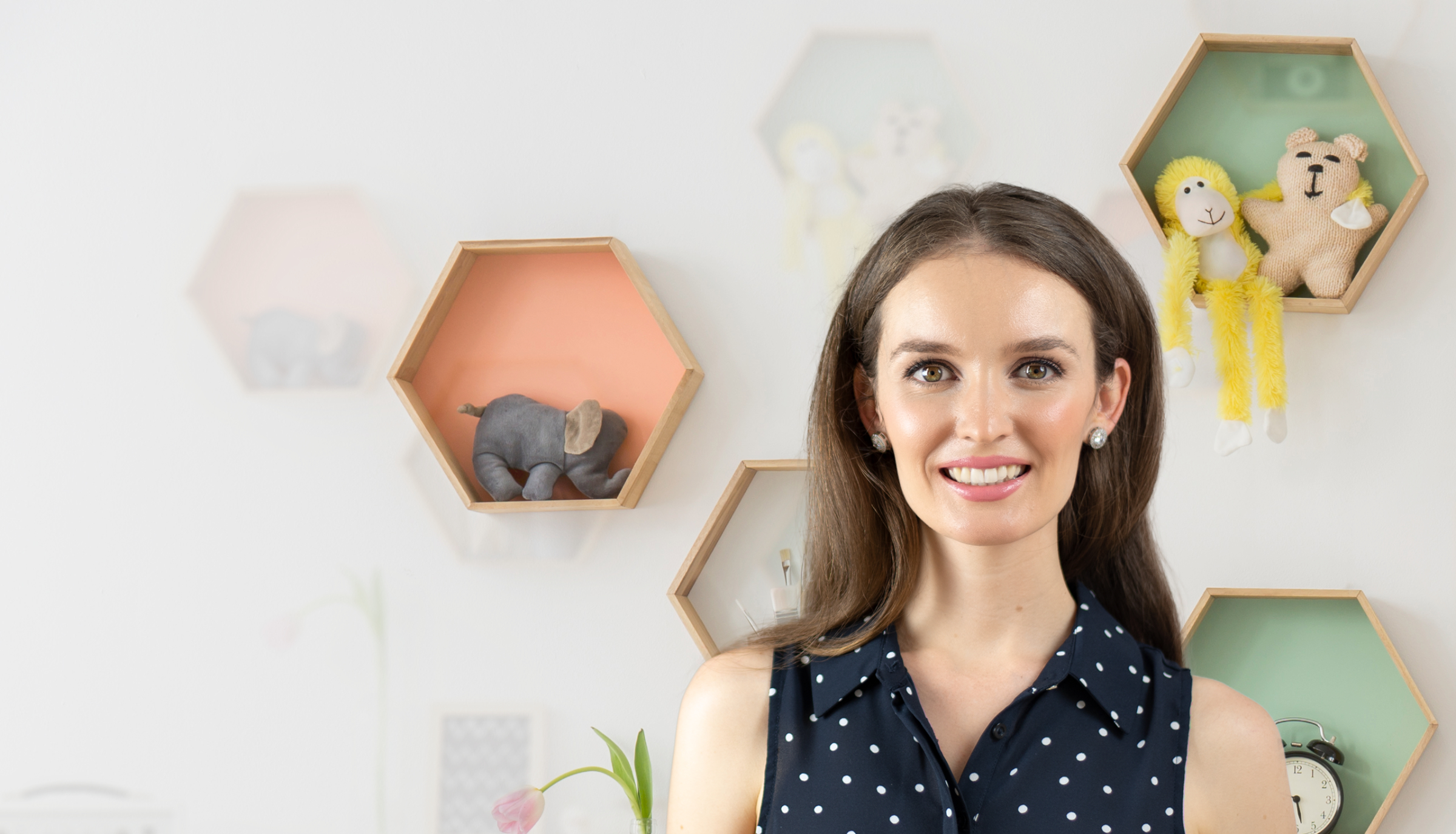 Speech pathologist Lauren Crumlish stands smiling in front of a wall with hexagonal shelves displaying stuffed toys.