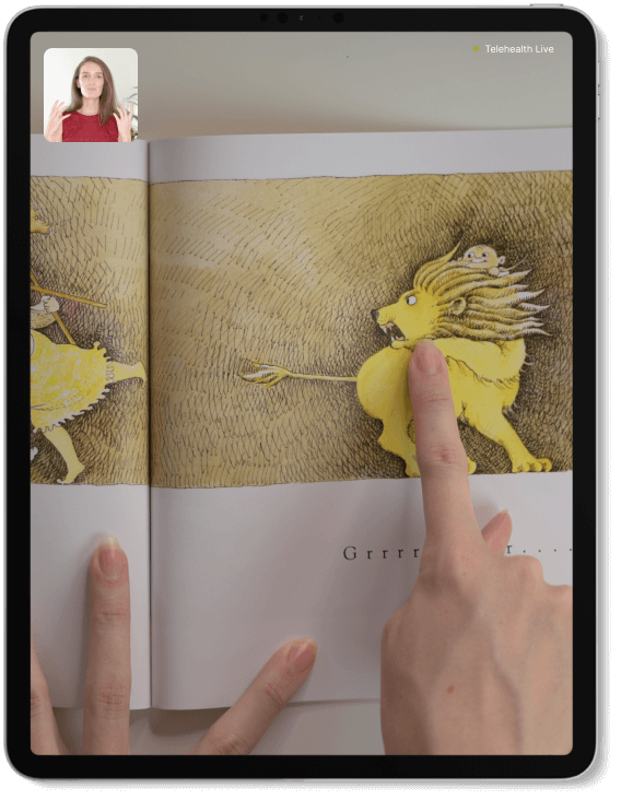 Lauren's hands hold and point to a picture book featuring an illustration of a lion and a person in a yellow dress. The word "Grrrrrrr" is partially visible.