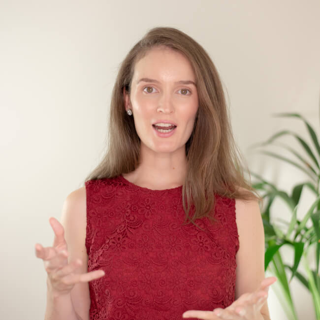 Speech Pathologist Lauren with her hands while speaking. A green plant is visible in the background.